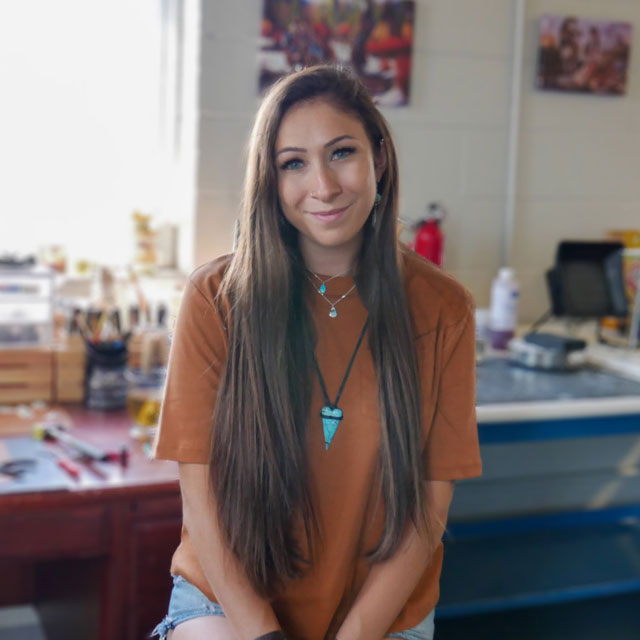 Woman with brown hair sitting in front of a workbench.